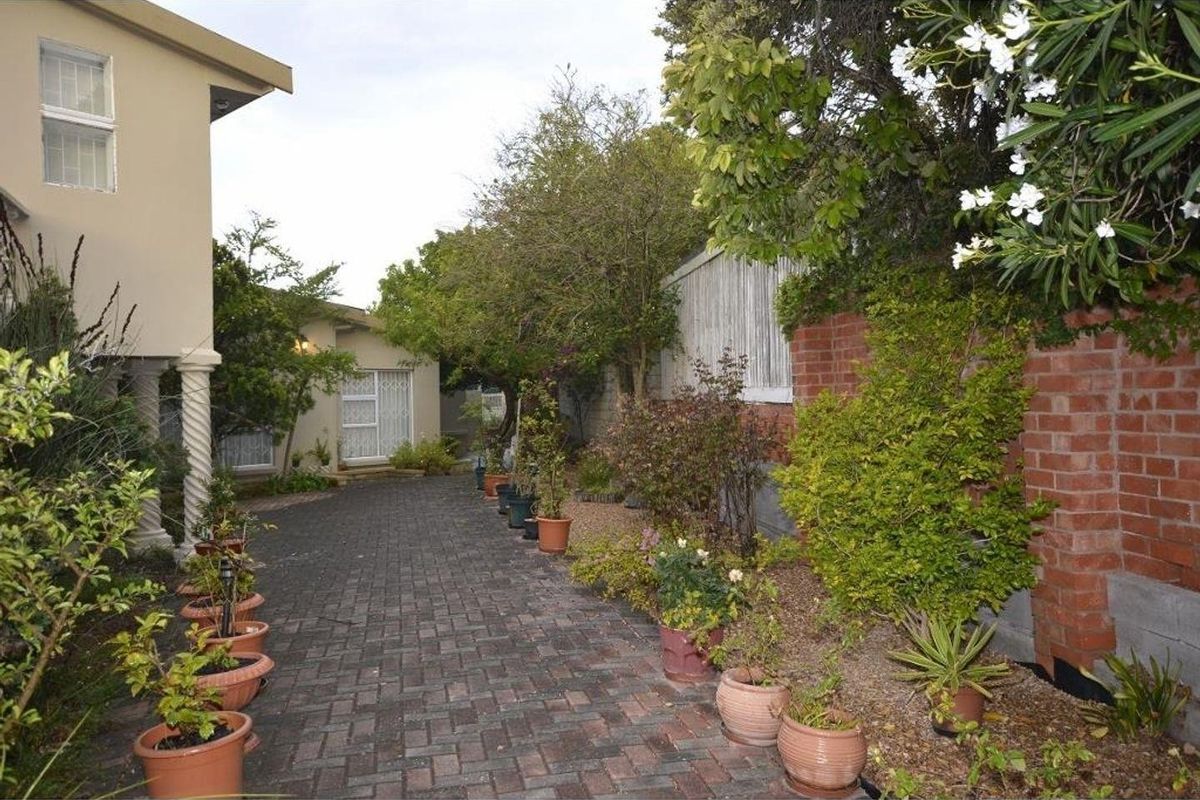 A paved rear courtyard area featuring a brick boundary wall, established garden beds, and access to the main dwelling via a sliding glass door.
