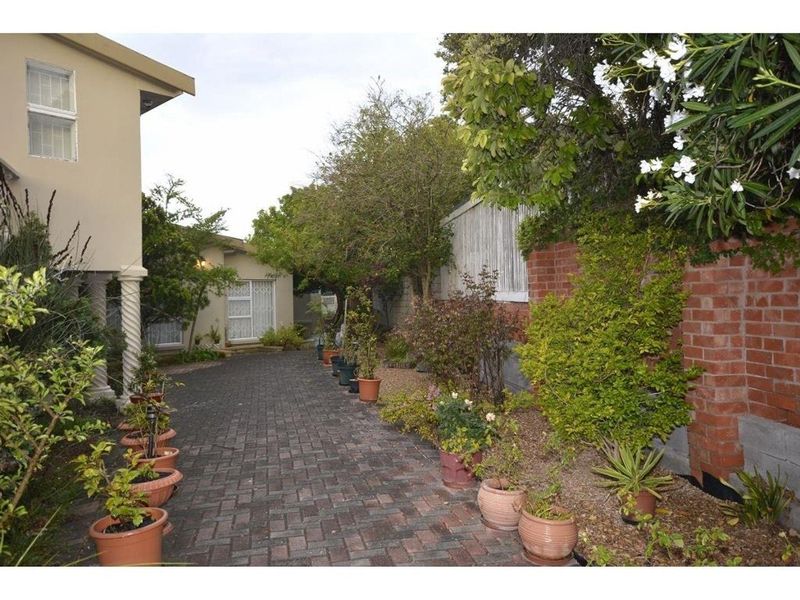 A paved rear courtyard area featuring a brick boundary wall, established garden beds, and access to the main dwelling via a sliding glass door.