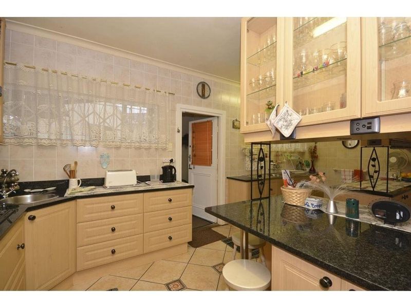 A functional kitchen featuring light wood cabinetry, dark granite countertops, tiled backsplash, and ceramic flooring with a breakfast bar area.