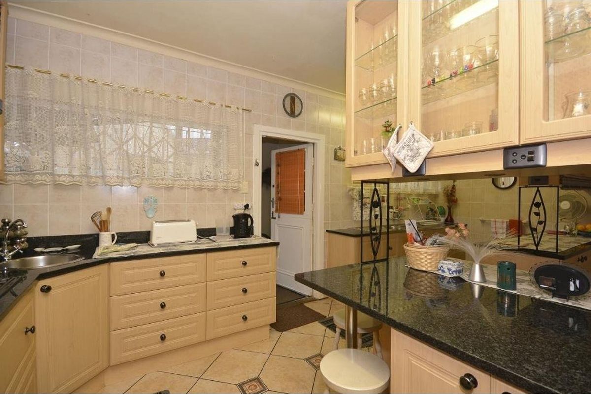 A functional kitchen featuring light wood cabinetry, dark granite countertops, tiled backsplash, and ceramic flooring with a breakfast bar area.