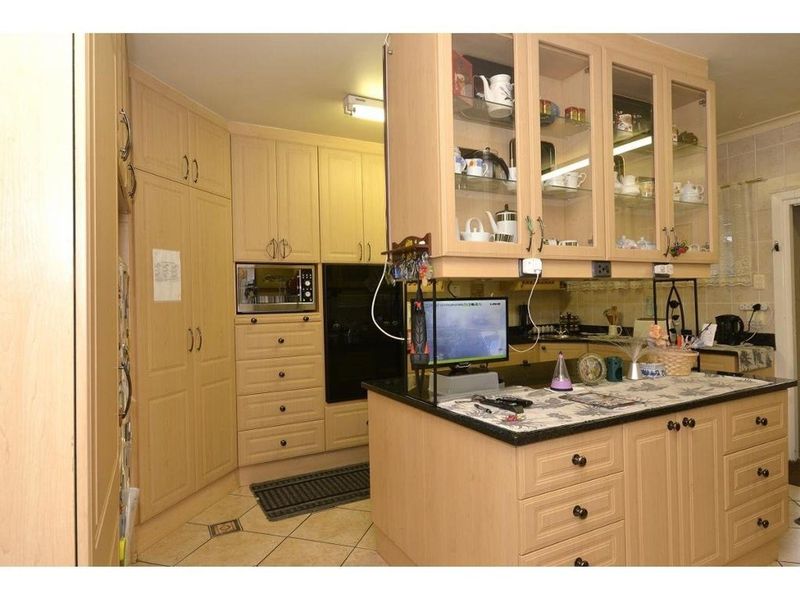 A functional kitchen featuring light wood cabinetry, granite countertops, built-in oven and microwave, and glass-front display cabinets with tiled flooring.