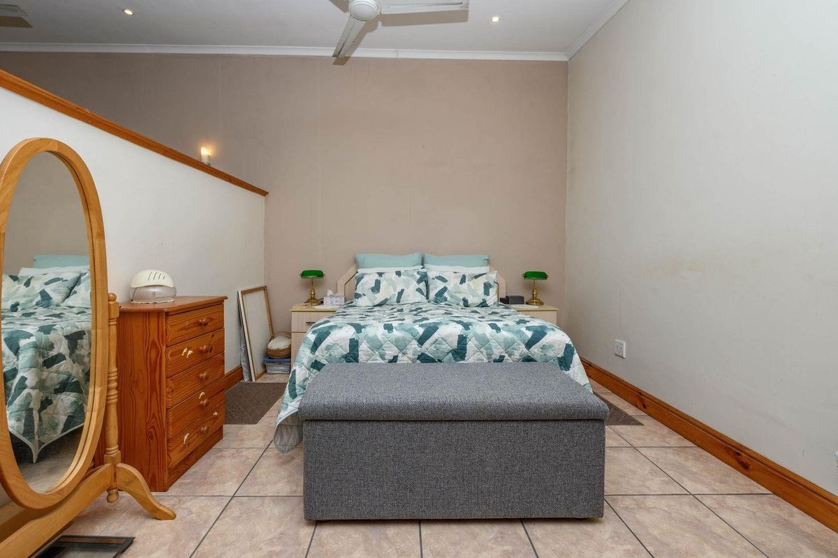 A bedroom featuring tiled flooring, timber skirting boards, and a ceiling fan, offering a functional space with neutral wall tones.