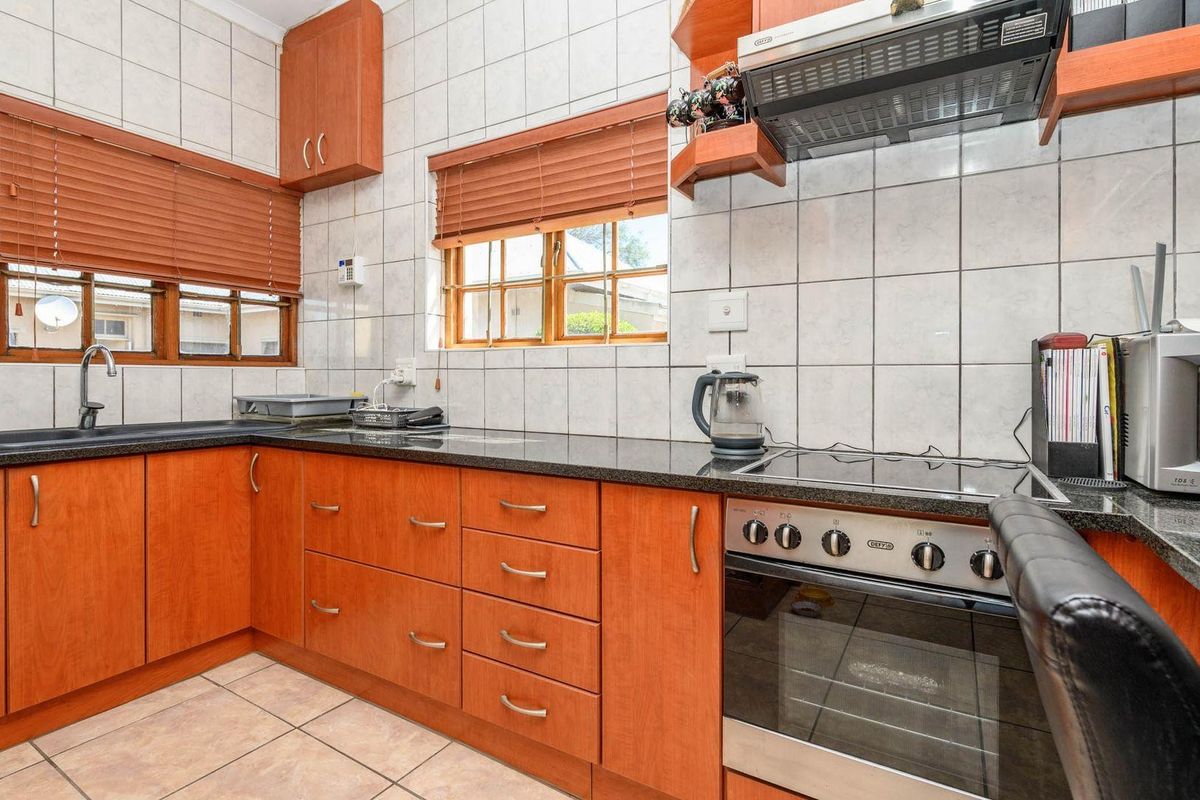 Functional kitchen featuring wood-look cabinetry, granite countertops, built-in oven with extractor fan, and tiled finishes throughout.