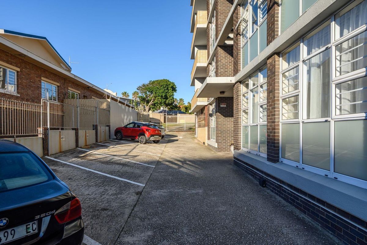 Rear exterior view of the apartment building featuring a concrete parking area, brick facade, and secure perimeter fencing.