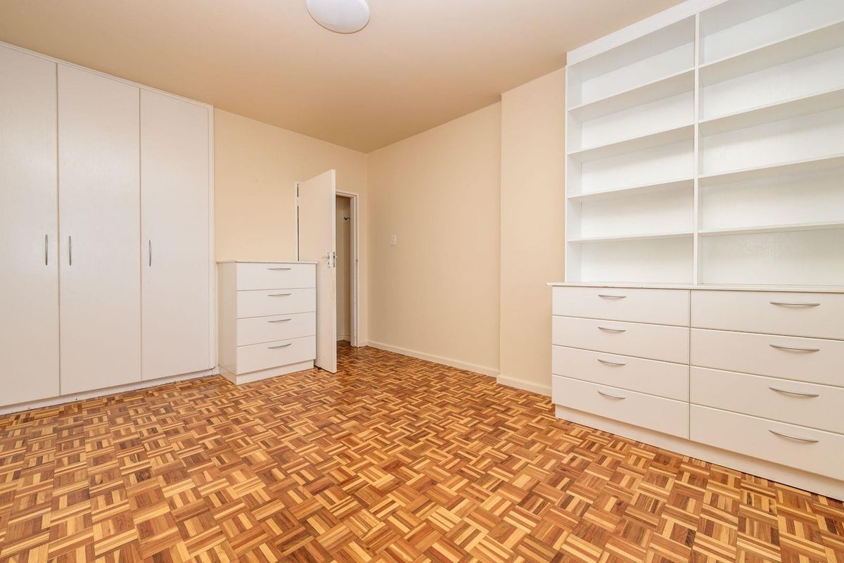 A bright bedroom featuring classic parquet flooring, extensive built-in cabinetry, and integrated shelving units, offering ample storage space in a clean, neutral setting.