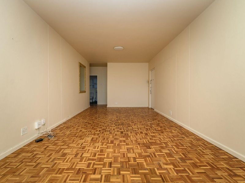 A spacious, empty living area featuring well-maintained parquet flooring and neutral wall finishes, offering a versatile blank canvas for interior design.