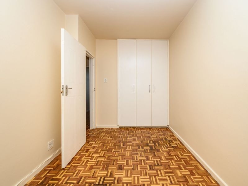 A clean, empty bedroom featuring classic parquet flooring and a built-in white wardrobe, offering a neutral canvas for personalization.