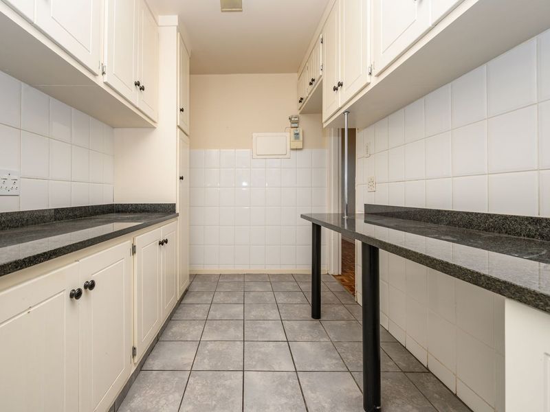 A functional scullery or utility area featuring ample built-in cabinetry, granite countertops, and tiled splashbacks, providing practical workspace and storage.