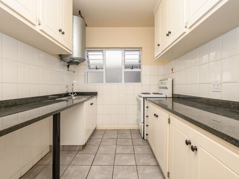 A functional galley-style kitchen featuring granite countertops, tiled backsplash, ample cabinetry, and a freestanding stove, offering a clean and practical workspace.