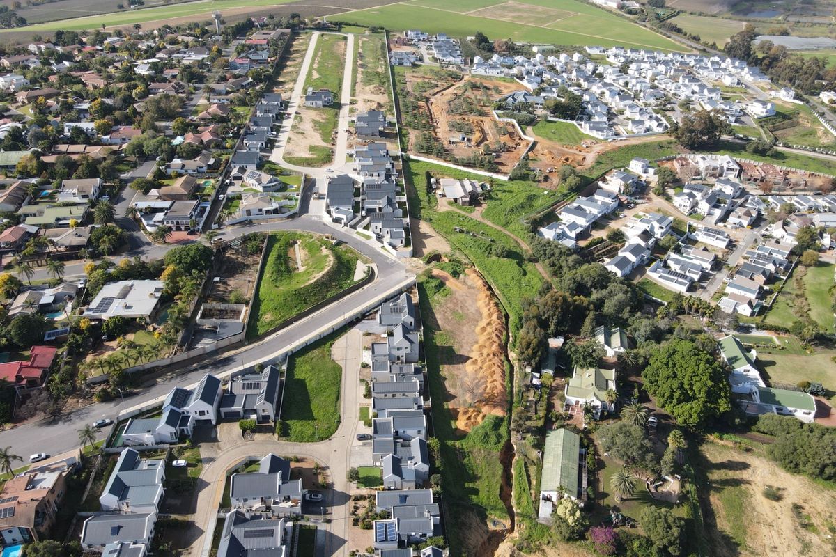 An aerial view of a residential estate featuring multiple housing units, paved road networks, and surrounding green spaces.