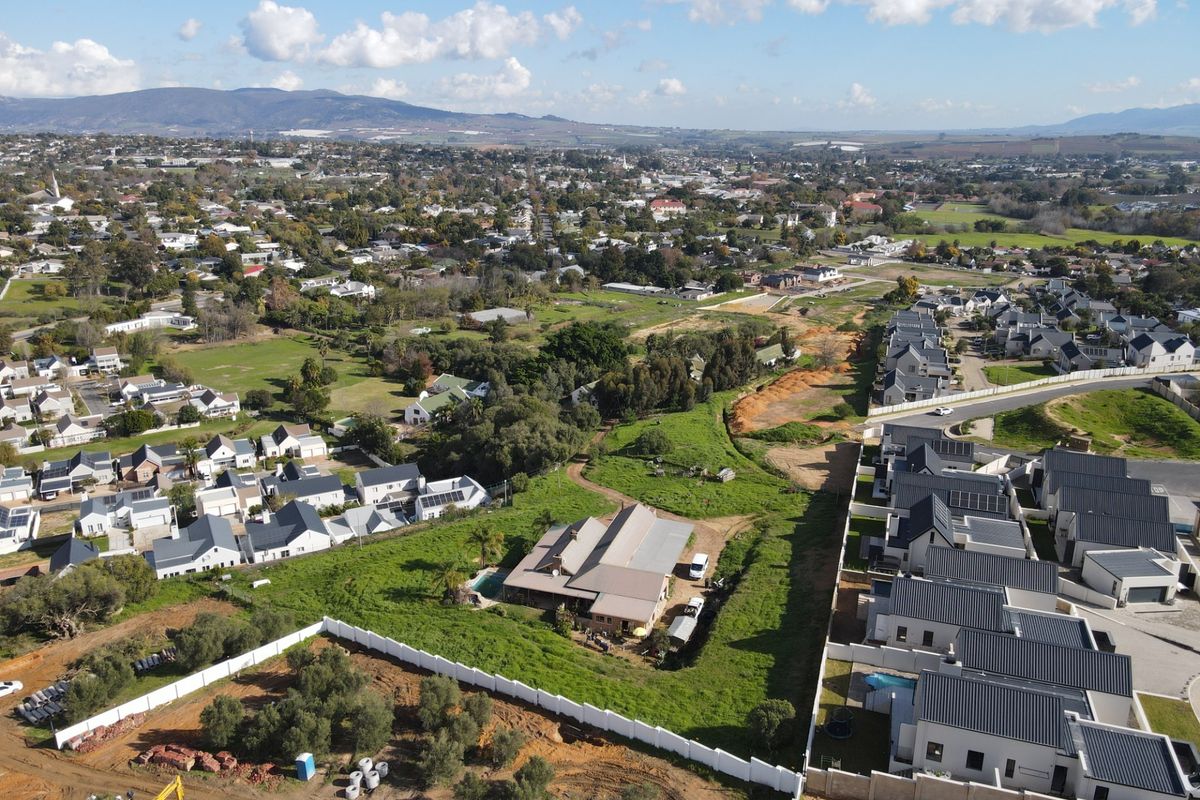 Aerial view of a residential property featuring a swimming pool, set within a suburban landscape with surrounding green spaces and neighborhood development.