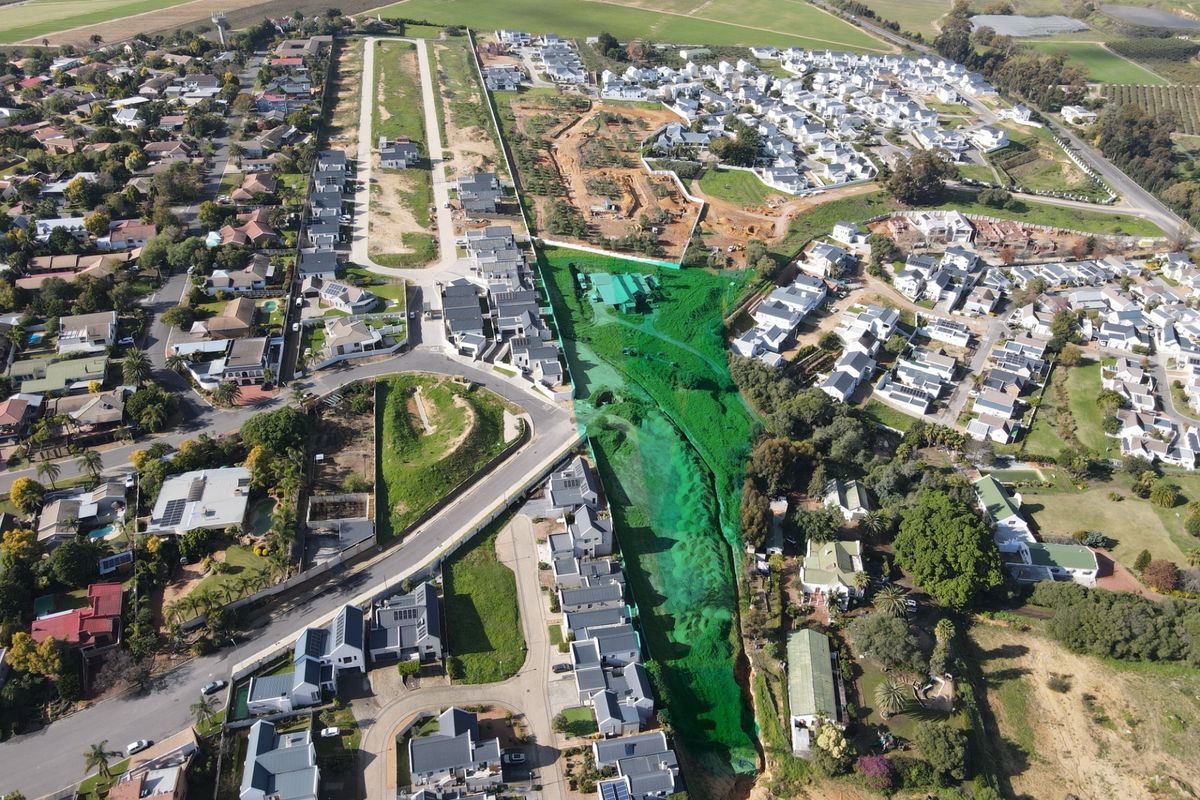 An aerial view of a residential estate featuring a central green belt, established road infrastructure, and surrounding suburban housing developments.