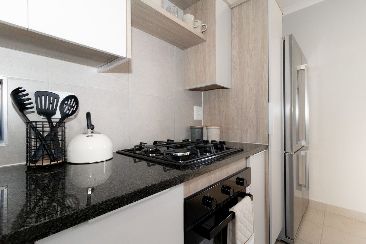Modern kitchen featuring granite countertops, built-in gas hob, integrated oven, and light wood-grain cabinetry with ample storage space.