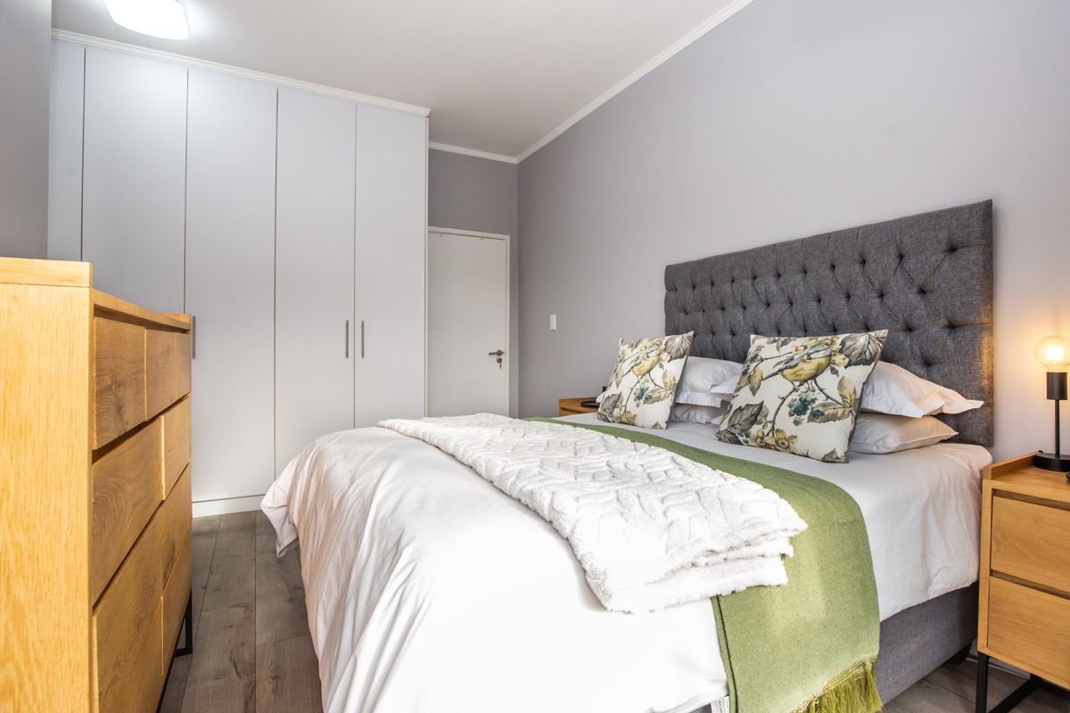A well-maintained bedroom featuring built-in floor-to-ceiling wardrobes, wood-look flooring, and neutral wall finishes.