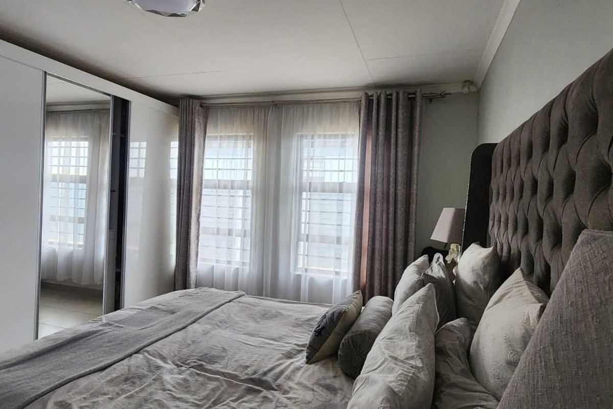 A well-lit bedroom featuring built-in sliding door wardrobes and large windows with security bars, providing a comfortable and functional living space.