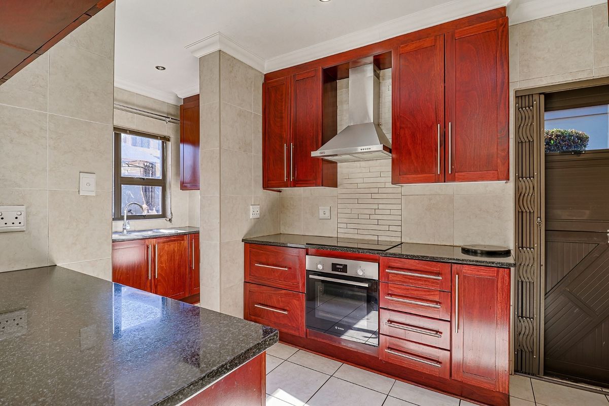 A well-maintained kitchen featuring dark wood cabinetry, granite countertops, a built-in oven, hob, and stainless steel extractor fan.