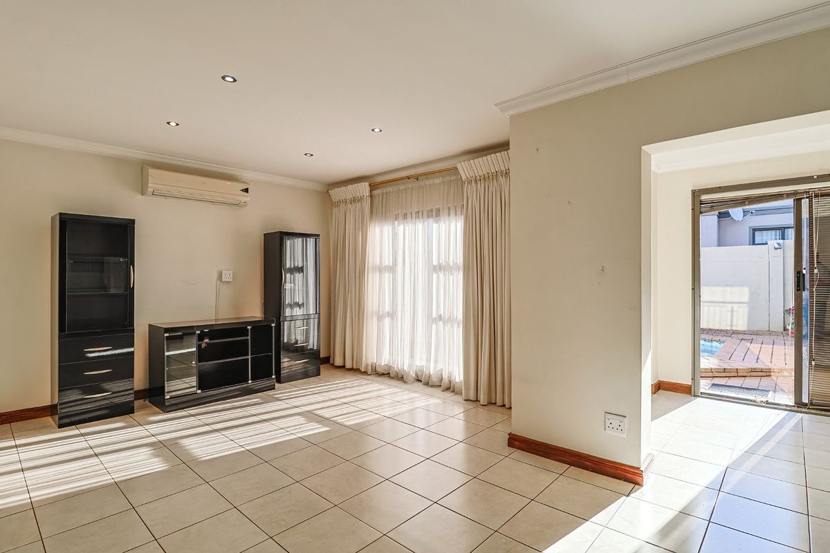 A bright living room featuring tiled flooring, recessed downlighting, and a wall-mounted air conditioning unit, with direct access to an outdoor patio area.