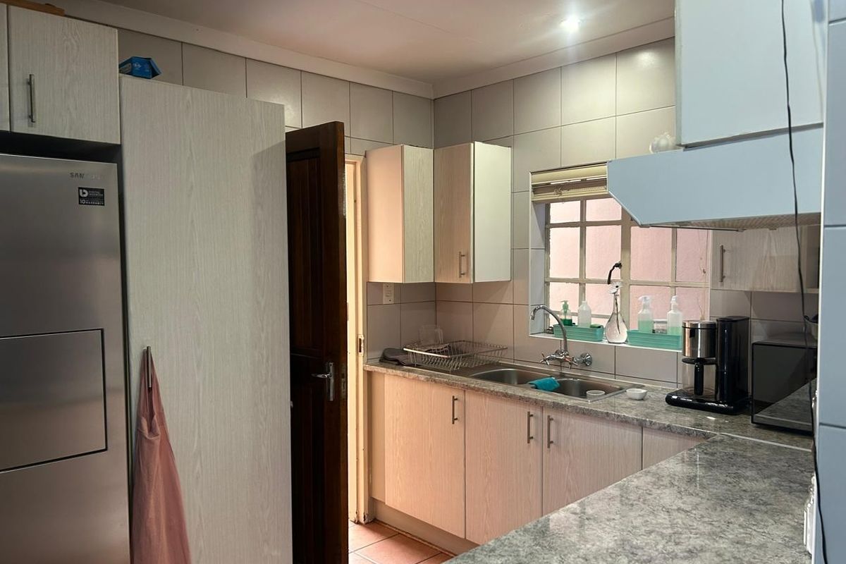 A functional kitchen featuring light wood-grain cabinetry, granite-look laminate countertops, a double basin sink, and tiled backsplash with an integrated extractor fan.