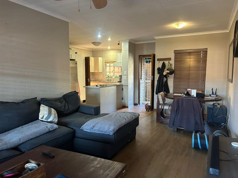 Open-plan living and dining area flowing into a functional kitchen with island, laminate flooring, and direct access to an exterior security gate.