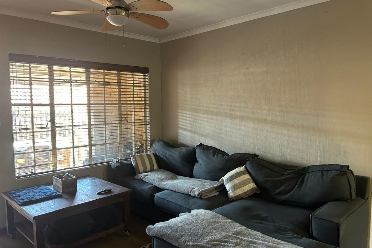 A living room featuring a ceiling fan and large window with venetian blinds, providing natural light and a functional layout.