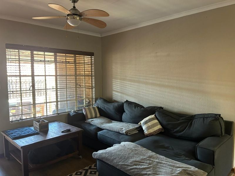 A living room featuring a ceiling fan and large window with venetian blinds, providing natural light and a functional layout.