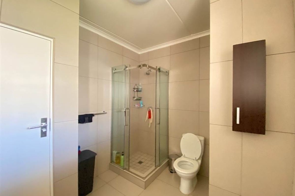 A functional bathroom featuring a glass-enclosed shower, a standard toilet, and neutral wall tiling throughout.