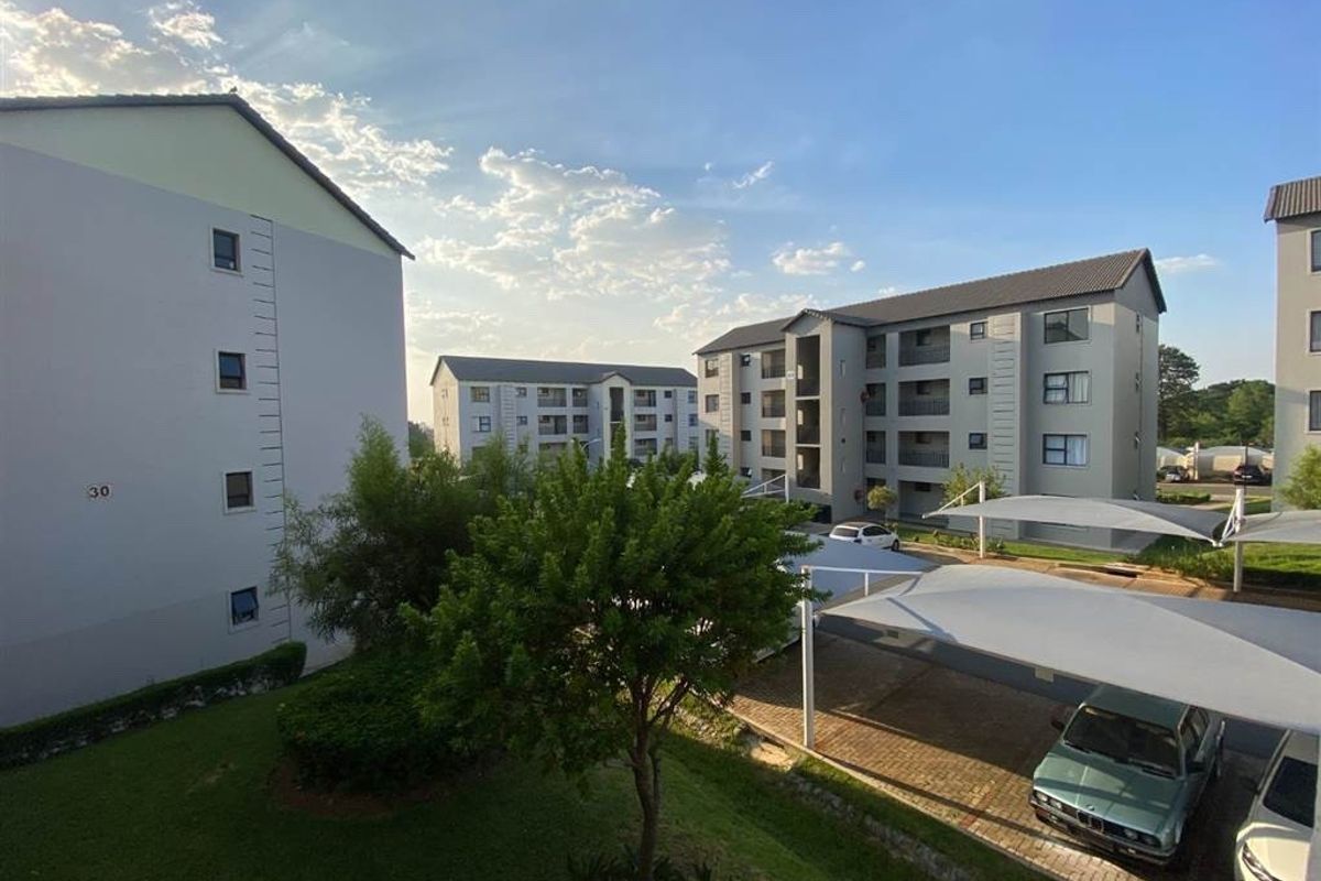 Exterior view of the apartment complex featuring multi-story residential buildings, landscaped garden areas, and covered parking bays for residents.