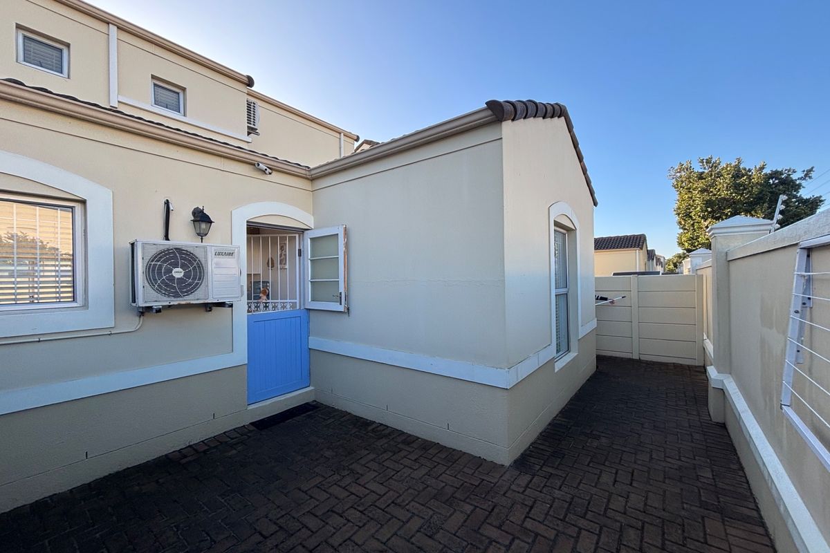 A paved rear courtyard area featuring a stable-style door, exterior air conditioning unit, and perimeter walling.