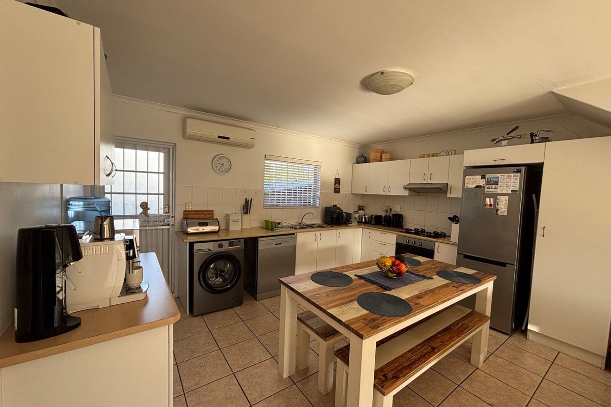 Functional kitchen featuring white cabinetry, tiled flooring, integrated appliances, and a dedicated dining area, with direct access to an exterior door.