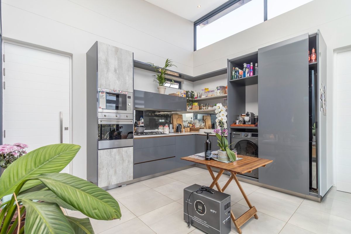 Modern kitchen featuring sleek grey cabinetry, built-in oven and microwave, integrated laundry appliances, and high ceilings with clerestory windows for natural light.
