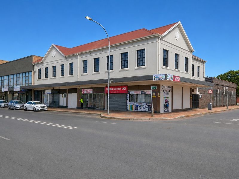 A corner commercial building featuring multiple ground-floor retail storefronts with security shutters and upper-level office or residential windows under a pitched roof.