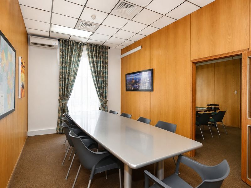 A professional office meeting room featuring wood-paneled walls, a suspended ceiling, and integrated air conditioning, providing a functional workspace for business operations.