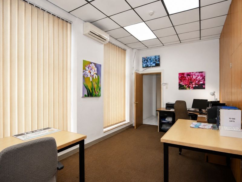 A functional commercial office space featuring a suspended ceiling, integrated air conditioning, vertical blinds, and built-in storage cabinetry.