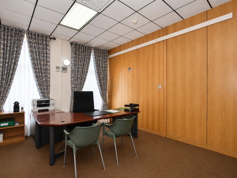 A functional commercial office space featuring wood veneer wall paneling, suspended ceiling tiles, and carpet flooring, suitable for professional use.