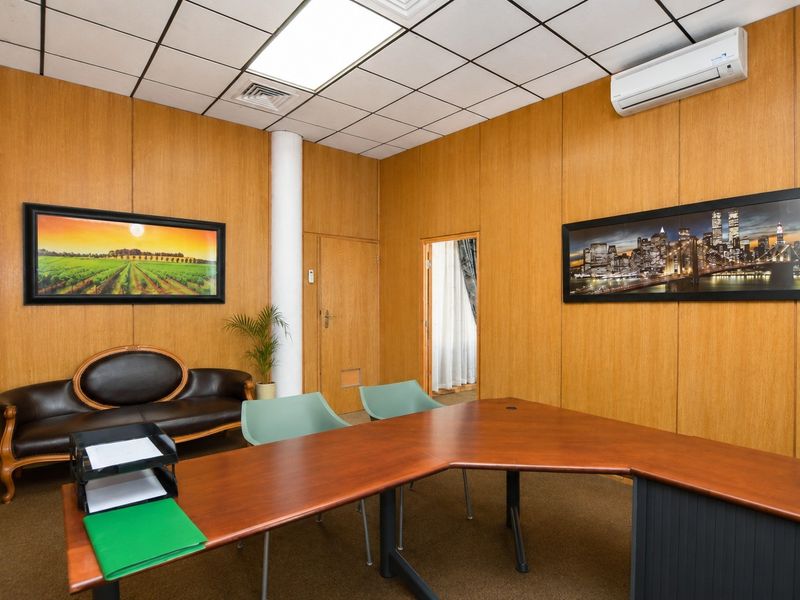 A professional office space featuring wood veneer wall paneling, suspended ceiling tiles, and a wall-mounted air conditioning unit.