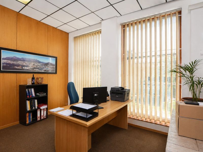 A professional office space featuring wood veneer wall paneling, suspended acoustic ceiling tiles, and large windows with vertical blinds.