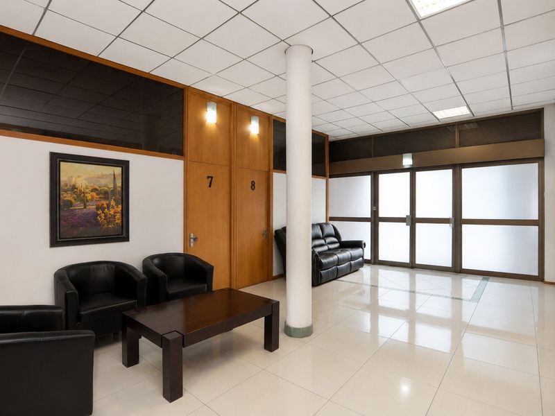 A professional commercial reception or waiting area featuring ceramic tiled flooring, a central structural column, and wooden office doors with frosted glass partitions.
