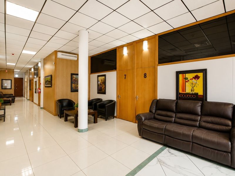 A commercial office hallway featuring wood-paneled walls, a suspended ceiling with recessed lighting, and polished ceramic floor tiles.
