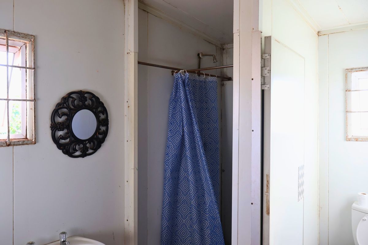 A dated bathroom featuring a shower stall, basic basin, and toilet, showing signs of wear and requiring cosmetic updates.