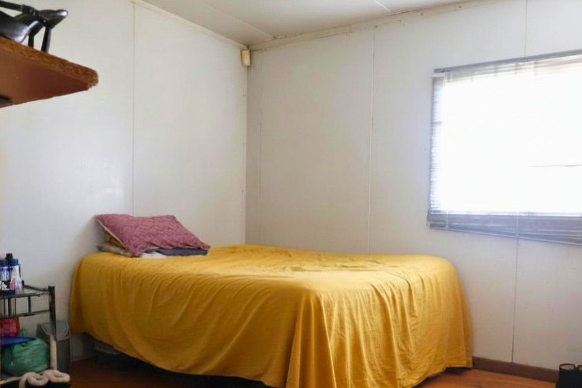A simple bedroom featuring basic wall paneling and a window with blinds, offering a functional space ready for cosmetic updates.