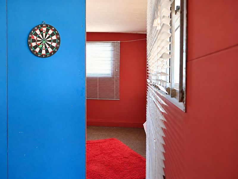 A bedroom space featuring bold red and blue wall finishes, fitted venetian blinds, and carpeted flooring.