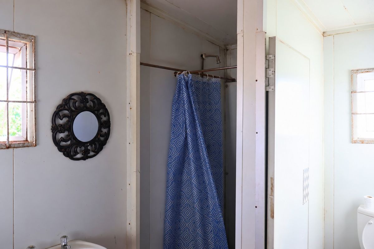 A dated bathroom featuring a shower area, toilet, and basin, showing signs of wear and requiring cosmetic updates to improve its condition.