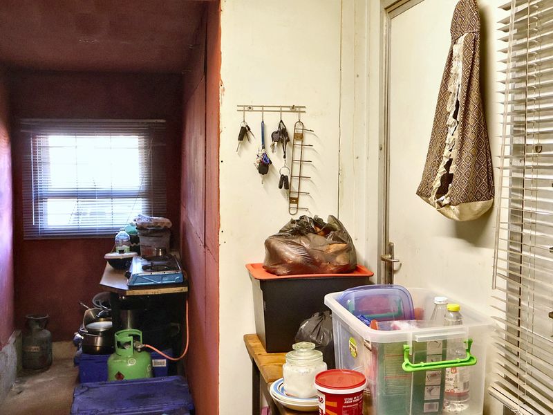 A narrow utility or storage area featuring basic wall finishes, a window with venetian blinds, and a functional access door.
