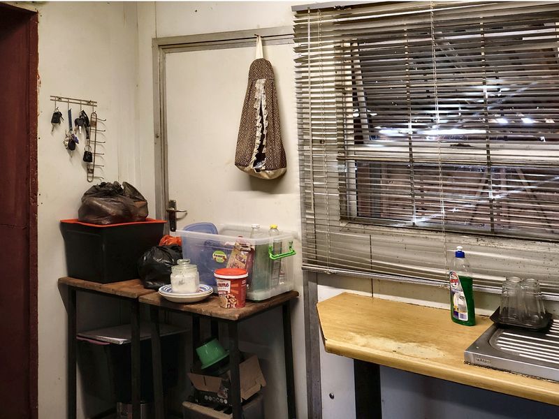 A functional scullery or utility area featuring a stainless steel sink, worn countertop, and window with venetian blinds.
