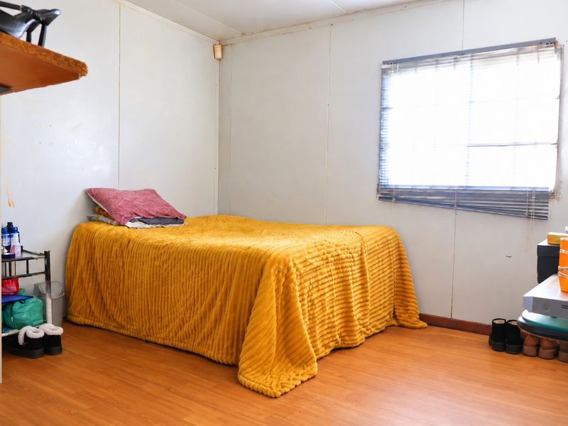 A bedroom featuring laminate flooring and a window with venetian blinds, requiring cosmetic updates to the wall finishes.