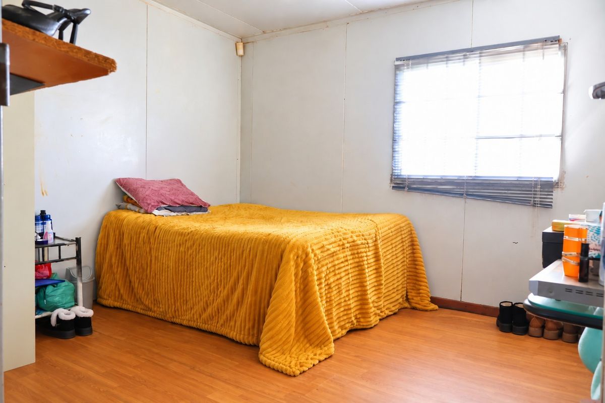 A bedroom featuring laminate flooring and a window with venetian blinds, requiring cosmetic updates to the wall finishes.