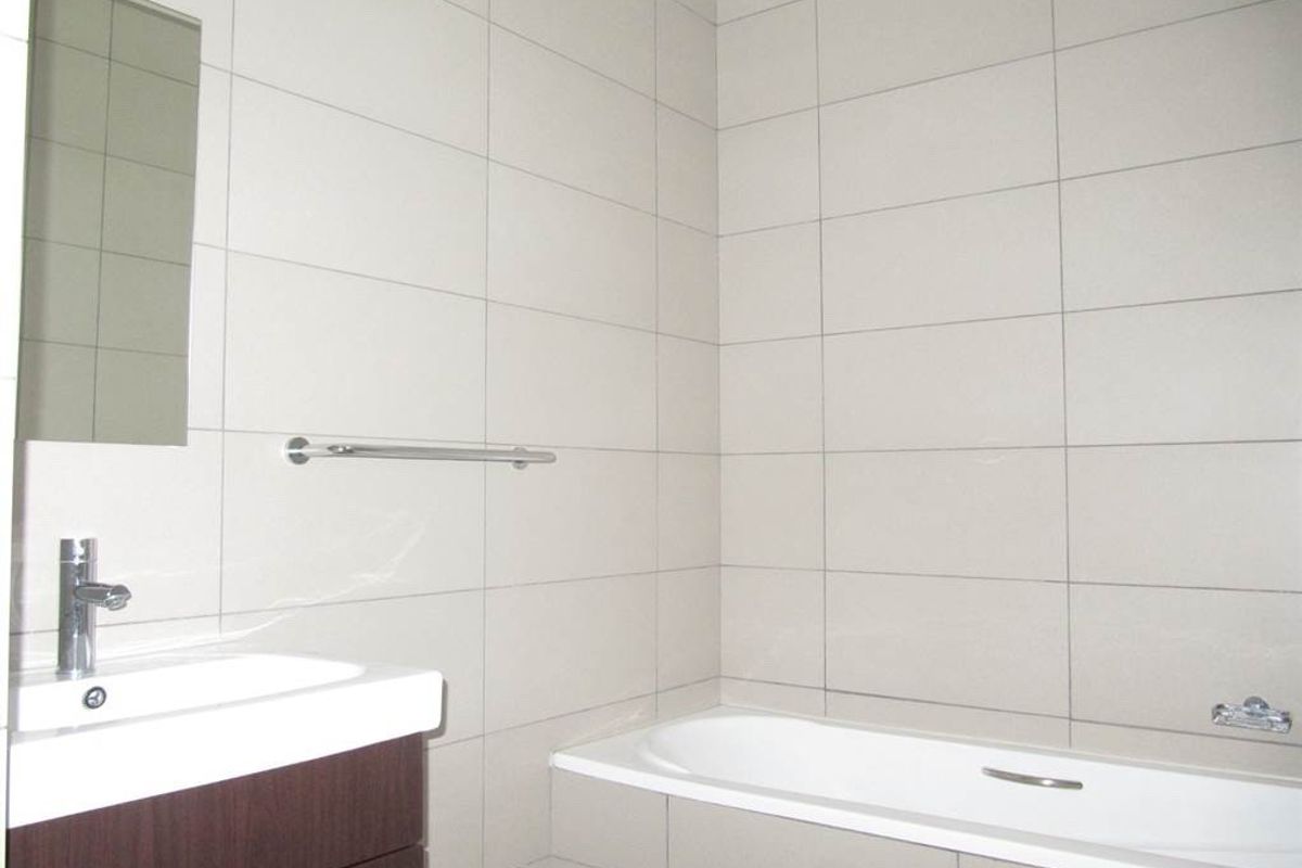 A modern bathroom featuring full-height wall tiling, a built-in bathtub, a vanity basin with storage, and a wall-mounted mirror.