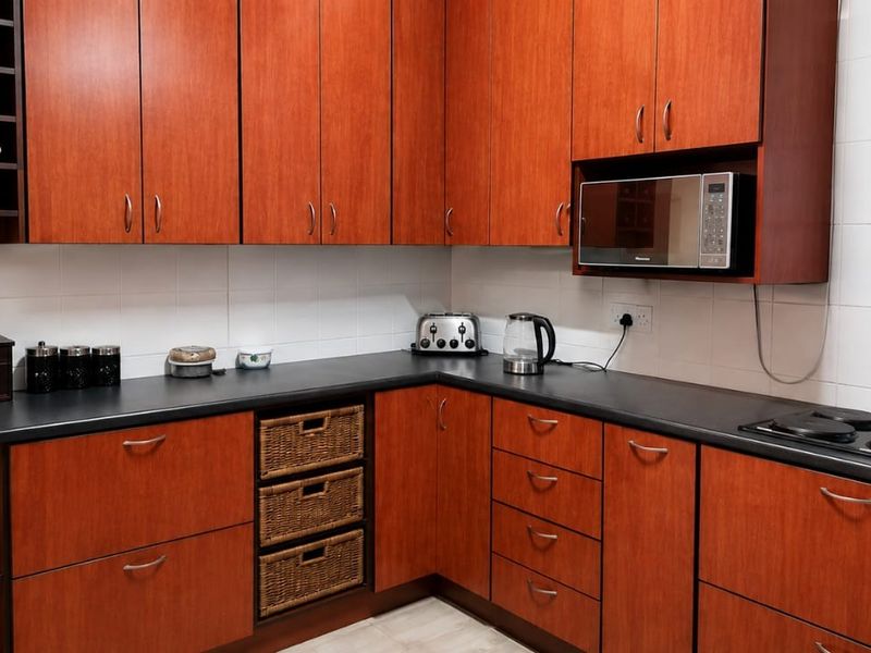 A functional kitchen featuring warm-toned wooden cabinetry, dark laminate countertops, a built-in microwave, and an integrated electric hob with tiled splashbacks.