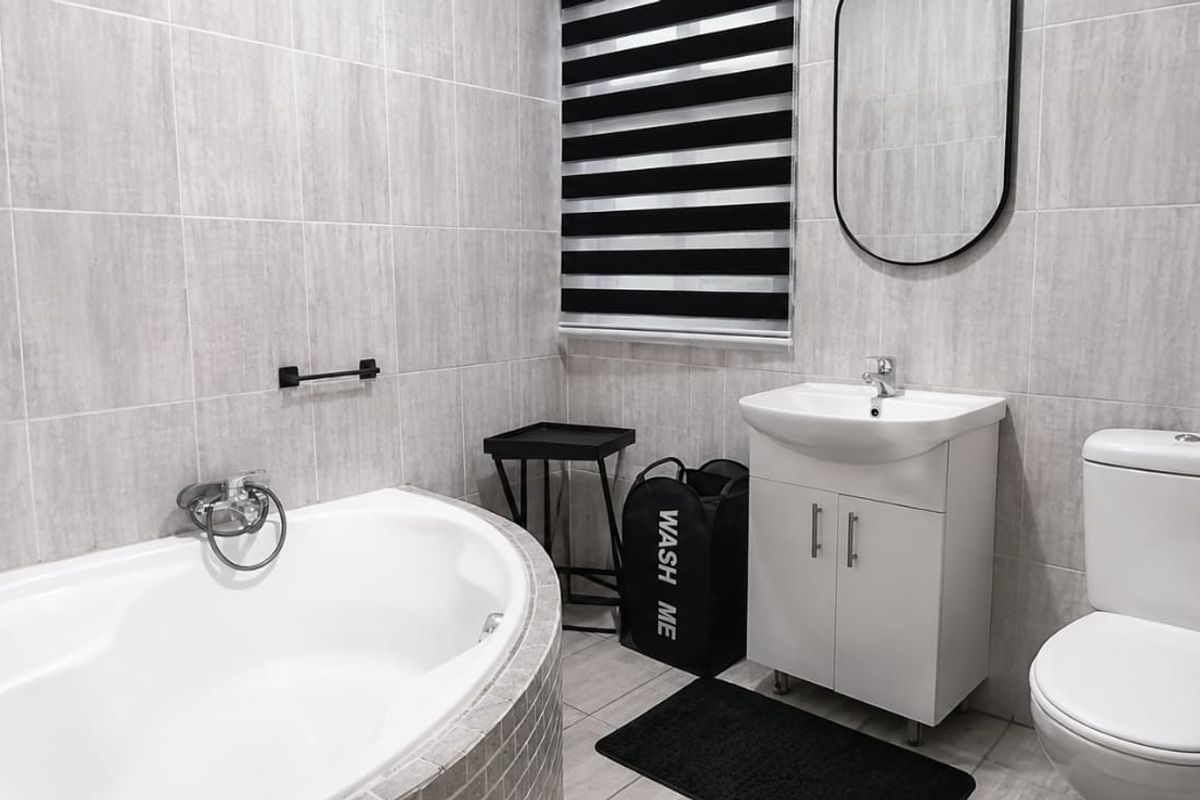 Modern bathroom featuring a built-in bathtub, vanity cabinet with basin, toilet, and neutral grey wall tiling.