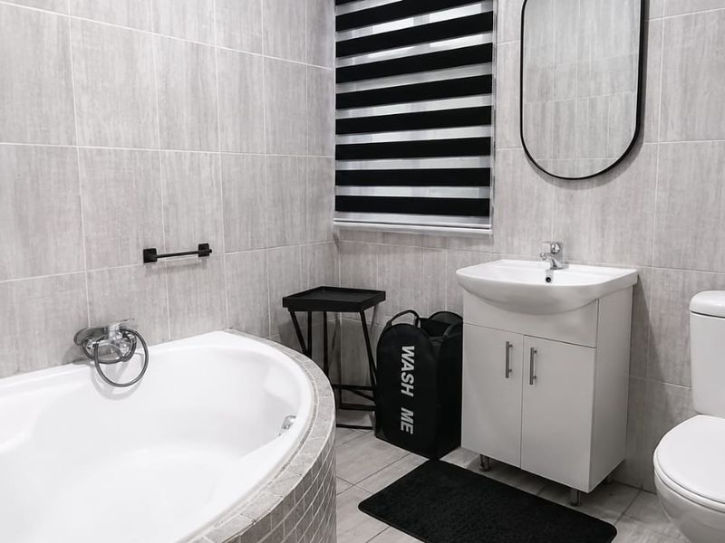 Modern bathroom featuring a built-in bathtub, vanity cabinet with basin, toilet, and neutral grey wall tiling.